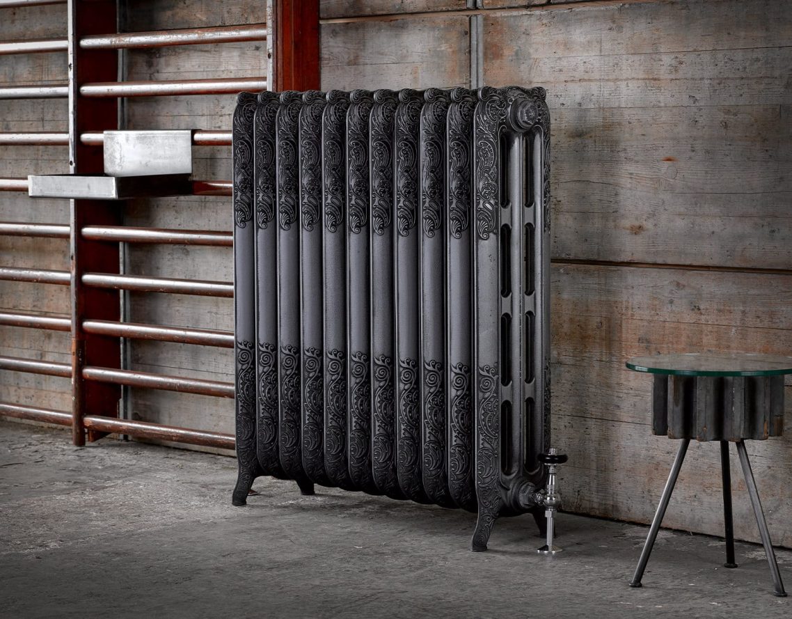 Aged Silver Polished Finish Black industrial radiator next to a small table against a textured concrete wall.