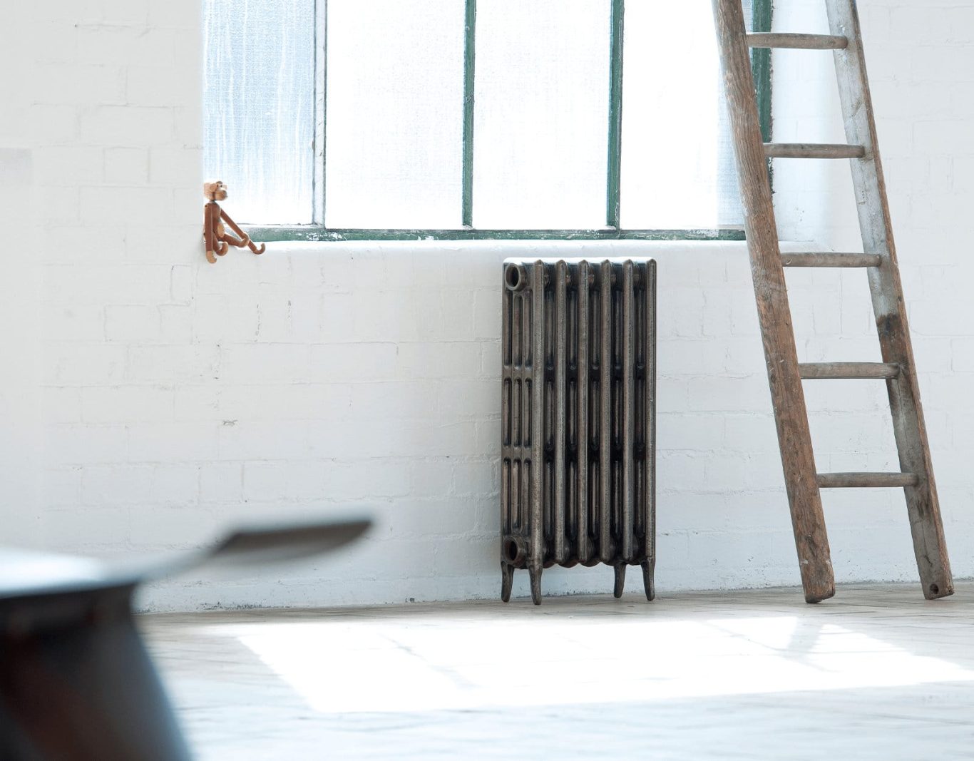 A metal radiator beside a wooden ladder in a bright room with a window.