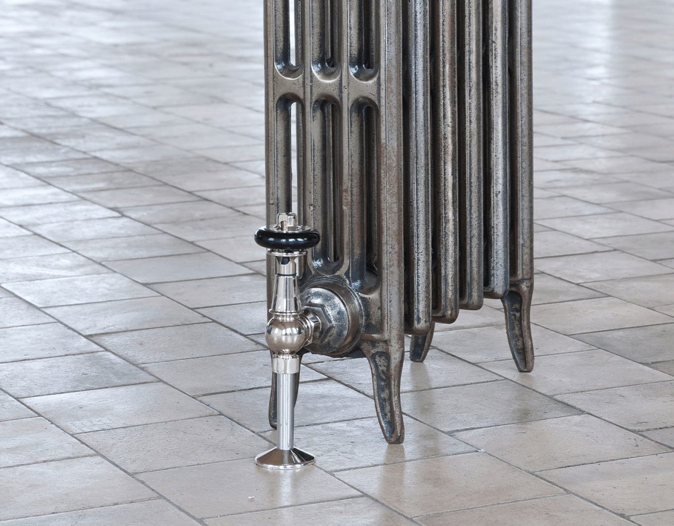 Metal radiator standing on a tiled floor, with a valve on the side.