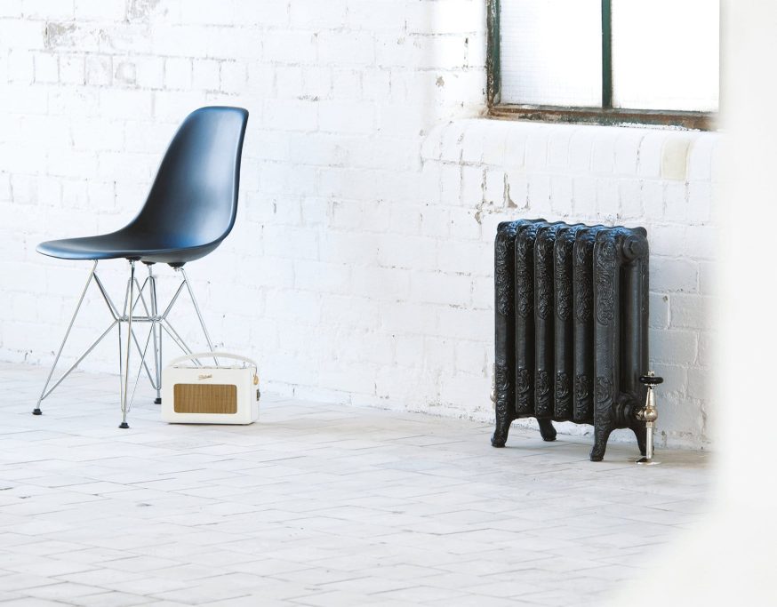 A black chair beside a black radiator and a vintage radio in a minimalistic space.